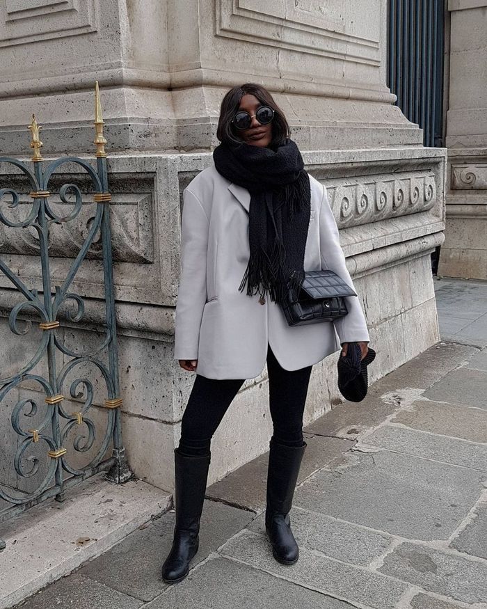 an oversized off-white blazer, black leggings, black riding boots, a black scarf and a bag for a trendy and contrasting look