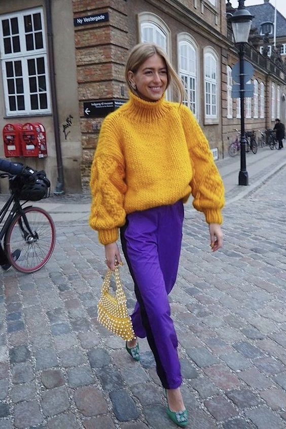 an oversized yellow turtleneck sweater, purple trousers, green embellished shoes, a yellow pearl bag