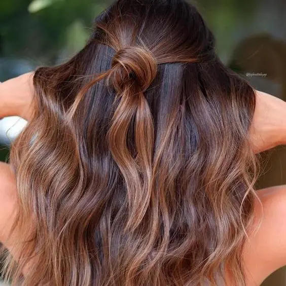 dark chestnut hair with waves and a knot and with caramel balayage to give the hair more dimension and texture