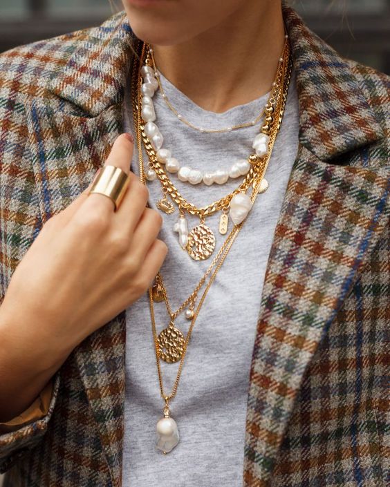 layered necklaces including usual and chunky chains, coins, baroque pearls and usual ones paired with a grey t shirt and a plaid blazer