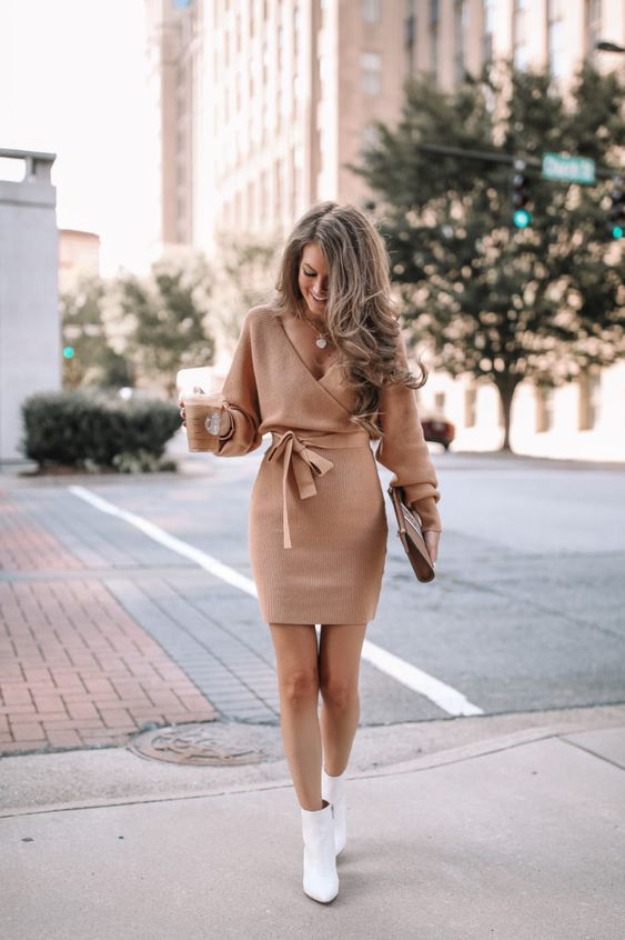 a beige mini sweater dress with a deep neckline, a sash and long sleeves, a nude clutch and white booties