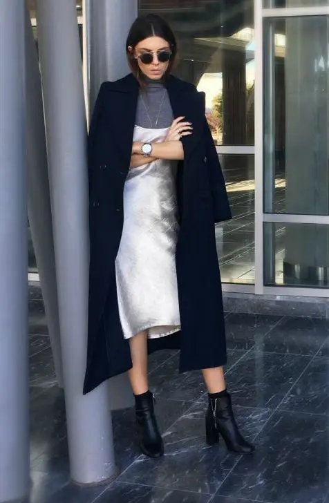 a layered outfit with a grey turtleneck, a white slip knee dress, a navy coat and black booties