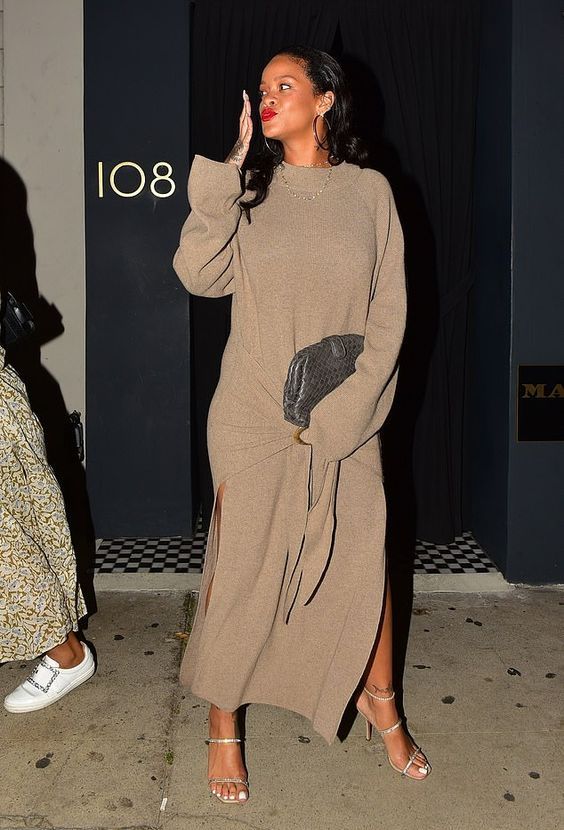 Rihanna wearing a beige knit maxi dress with long sleeves and a high neckline, wide slits, silver shoes and a graphite grey bag