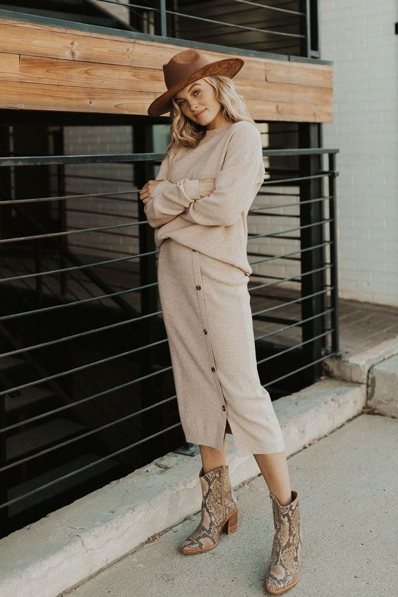 a knit co-ord set with a neutral jumper and a button up midi skirt, snakeskin print boots and a brown hat