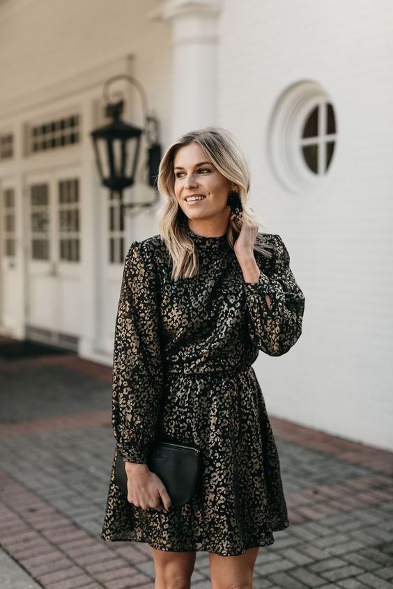 a black and silver printed mini A line dress with a high neckline and long sleeves, a black bag and black statement earrings