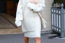 20 Hailey Bieber wearing a tan top, a white ribbed skirt and a matching oversized cardigan, grey boots and a bag