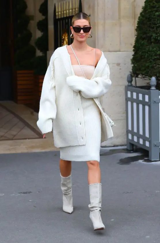 Hailey Bieber wearing a tan top, a white ribbed skirt and a matching oversized cardigan, grey boots and a bag