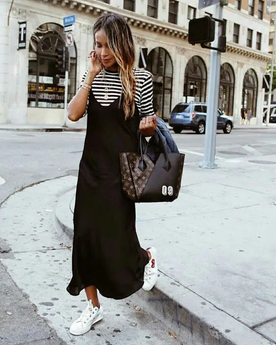 a pretty spring work outfit with a striped short sleeve top, a black slip midi dress, white sneakers and a printed tote