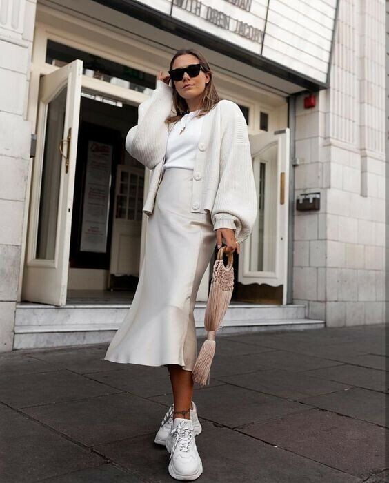 a stylish neutral work look with a white t-shirt, a slip mermaid skirt, white trainers, a white chunky cardigan with puff sleeves