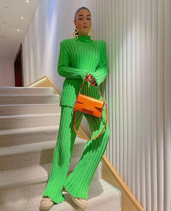 a bright winter look with an apple green ribbed jumper and pants, neutral boots, an orange bag and statement earrings