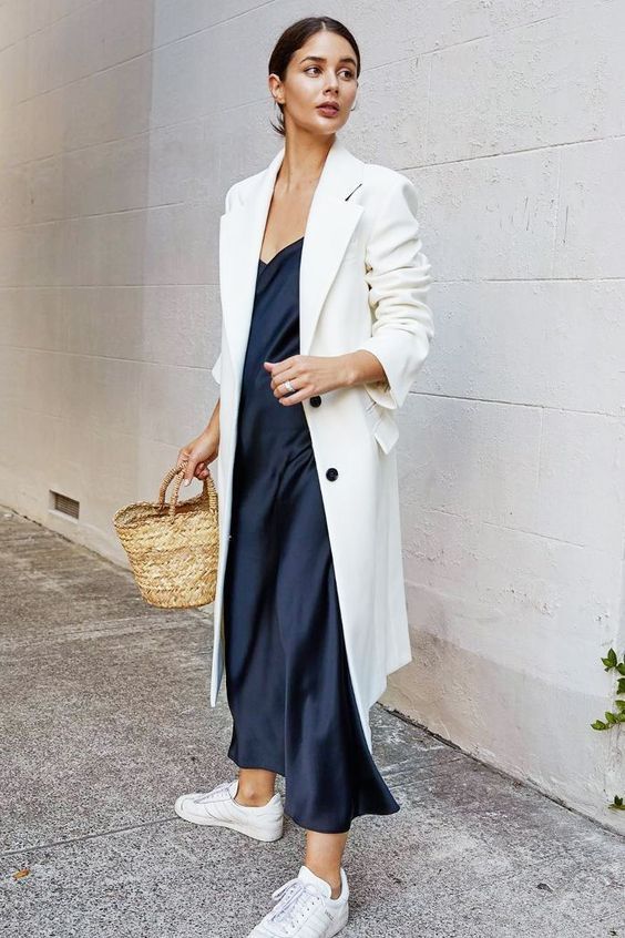 a navy slip midi dress, a white trench, white sneakers and a straw bag for a spring work outfit