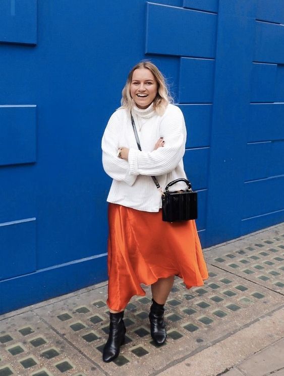 a simple fall work look with an oversized white sweater, an orange slip midi, black boots, a black bag