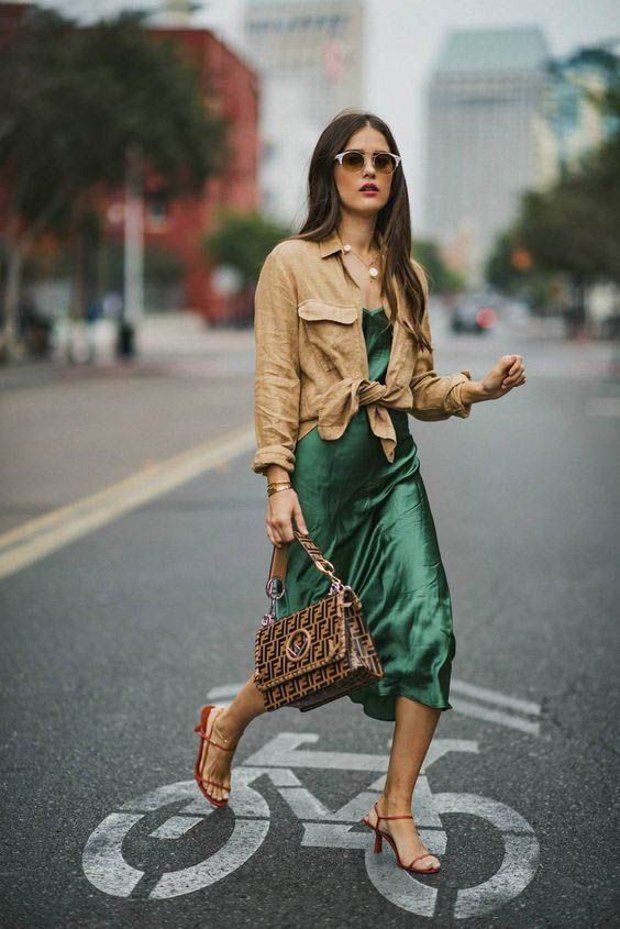 a creative summer work look with a green slip midi dress, a linen tan shirt over it, red heels and a printed bag