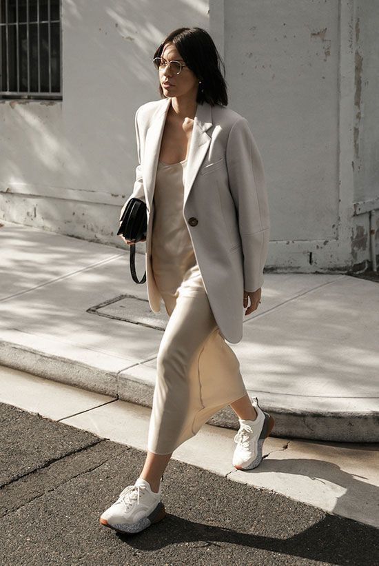 a minimalist summer work outfit with a white slip midi dress, a matching oversized blazer, white trainers and a black bag
