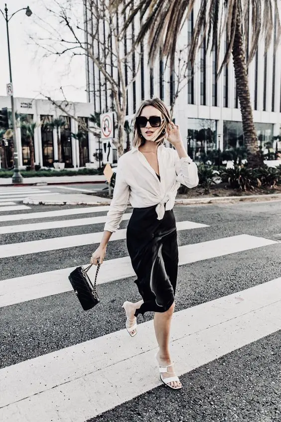 a refined monochromatic summer work look with a black slip midi dress, a white shirt over it, white whimsy heels and a black bag