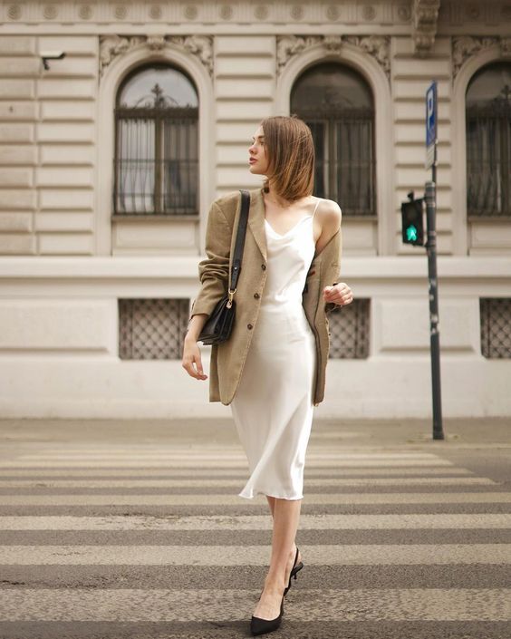 a simple and chic work outfit with a white slip midi dress, black slingbacks, a beige oversized blazer and a black bag