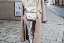a creamy oversized sweater, a silver sequin midi skirt with a front slit, grey trainers and a nude trench