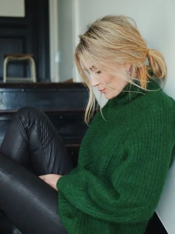 a messy yet chic holiday look with a green turtleneck sweater, black leather pants and statement earrings