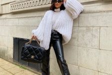 a neutral turtleneck, an oversized white chunky cardigan, black leather pants, black boots and a black quilted bag