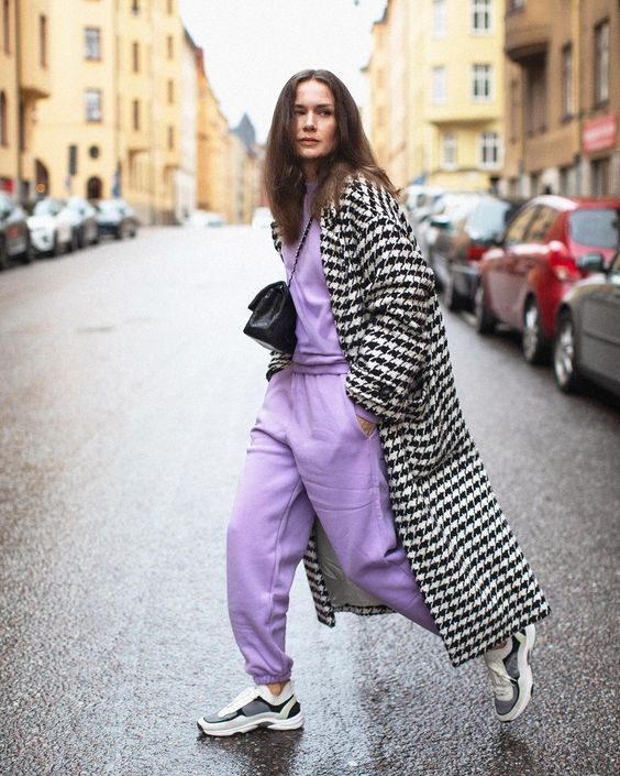 a periwinkle sweatshirt and sweatpants, grey and white trainers, a black and white printed midi coat and a black bag