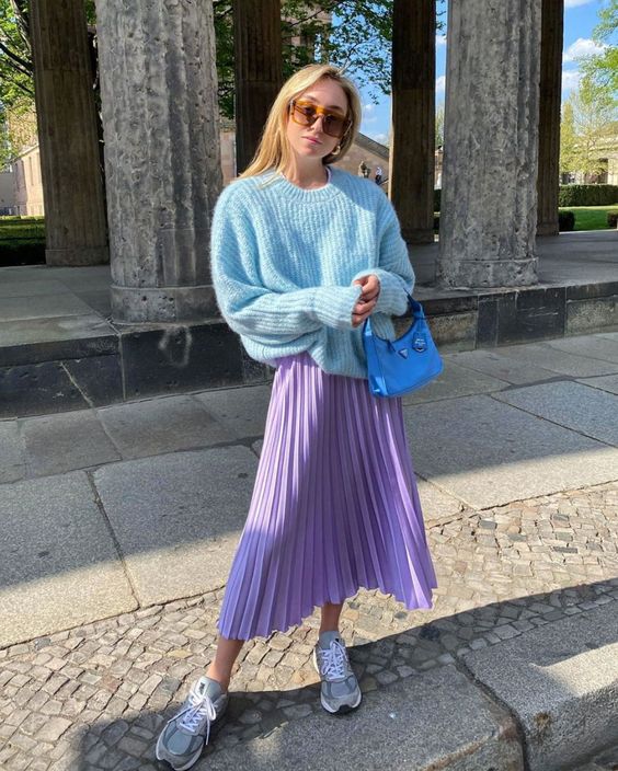 a spring look with an aqua blue chunky knit sweater, a periwinkle pleated midi, grey trainers and a bold blue bag