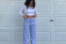 a spring outfit with a white crop top with long sleeves, periwinkle high waisted jeans, creamy boots and a small bag