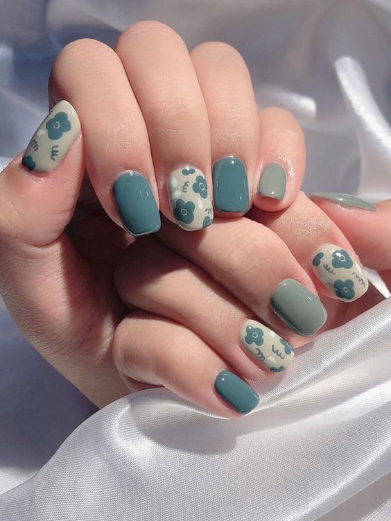 mismatching green and blue nails of muted shades, with floral print accents are amazing