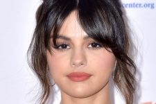 Selena Gomez wearing dark shiny hair in a messy top knot and layered bangs looks gorgeous and elegant
