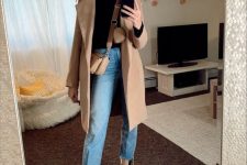 a black turtleneck, blue jeans, two-tone boots, a tan coat and a tan crossbody bag compose a simple yet bold look