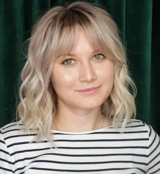 a blonde medium length hairstyle with a darker root, bottleneck bangs and waves is a lovely idea to try