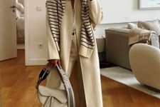 a chic all-neutral outfit with a white shirt and trousers, a coat and a striped sweater on top, neutral sneakers and a bag