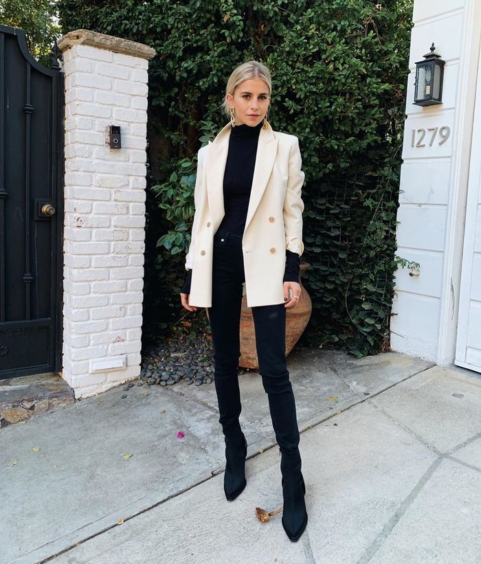 a chic and contrasting look with a black turtleneck, black boos, jeans and a white blazer plus statement earrings
