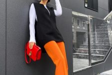 a white long sleeve top, a black woolen waistcoat, orange pants, black shoes and a bright red bag