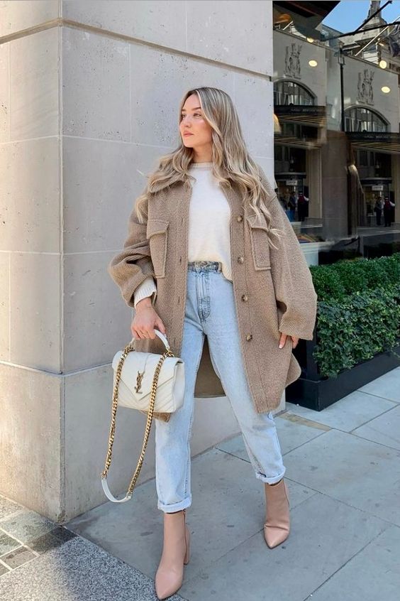 a white sweater, a tan shirt jacket, light blue jeans, blush boots, a white bag with chain for colder days