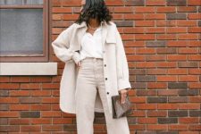 an all-neutral outfit with a white shirt, off-white high waisted jeans, white boots, a neutral shirt jacket and a clutch