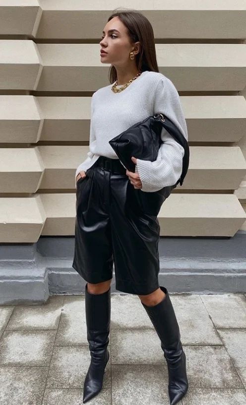 an edgy work outfit with a white oversized sweater, black leather shorts, black boots and a bag