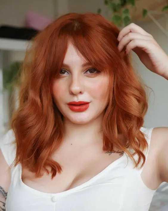bold ginger medium length hair with bottleneck bangs and a lot of volume and waves is a chic and catchy idea