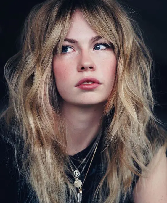 long blonde wavy hair with bottleneck bangs and a lot of volume looks very messy, chic and sexy