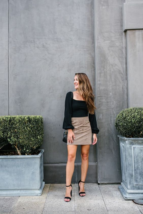 a black top with a square neckline and puff sleeves, a tan mini skirt, black shoes and a black bag