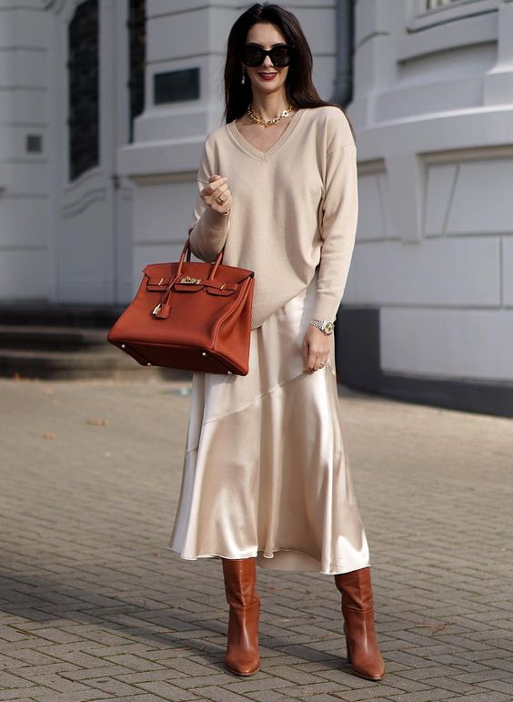 a neutral jumper, a neutral slip midi skirt, brown boots, a brown tote and a chain necklace for work