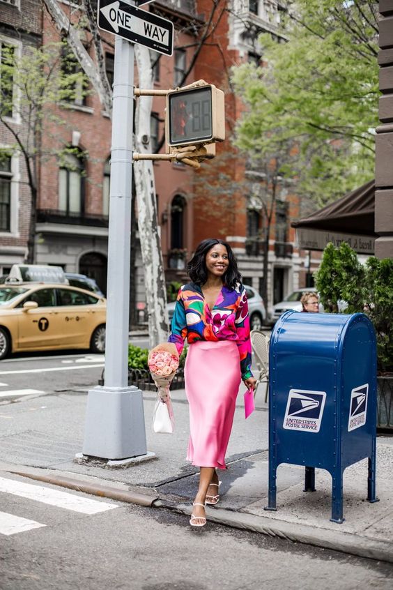 a colorful look with a bold blouse, a pink slip midi skirt, white strappy shoes and a hot pink clutch