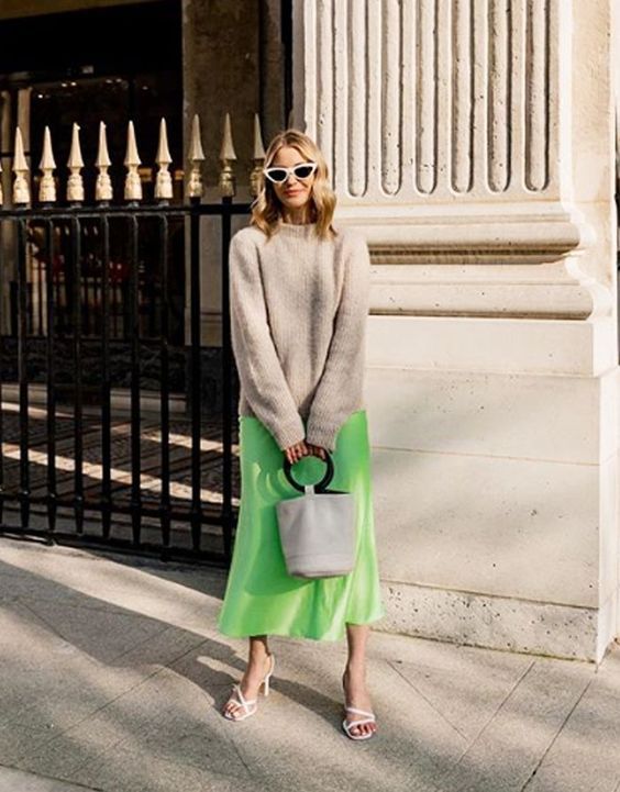 a tan jumper, a neon green slip midi skirt, white strappy heels, a white bucket bag and cool sunglasses