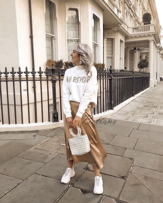 a white printed jumper, a gold midi slip skirt, white trainers and a white bag with round handles