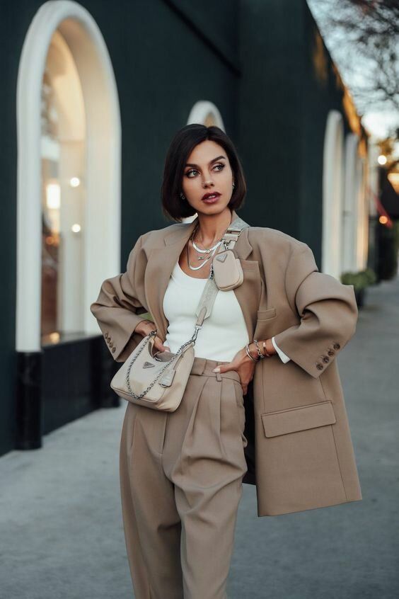 a stylish greige pantsuit with an oversized blazer, a white top, a grey bag and layered necklaces
