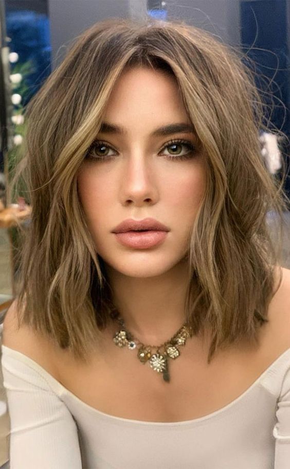 a soft and delicate light brunette shoulder-length bob with warm blonde balayage and messy waves is chic