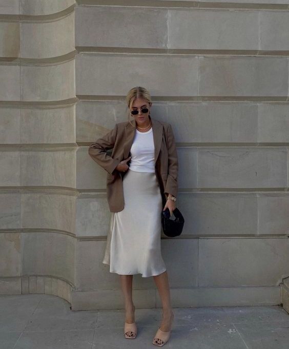 a white top, a creamy slip midi skirt, tan heeled mules, a taupe oversized blazer and a black bag for a contrast