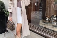 24 a girlish outfit with a taupe turtleneck, a white pleated mini, tan knee boots, a grey trench and a brown printed bag