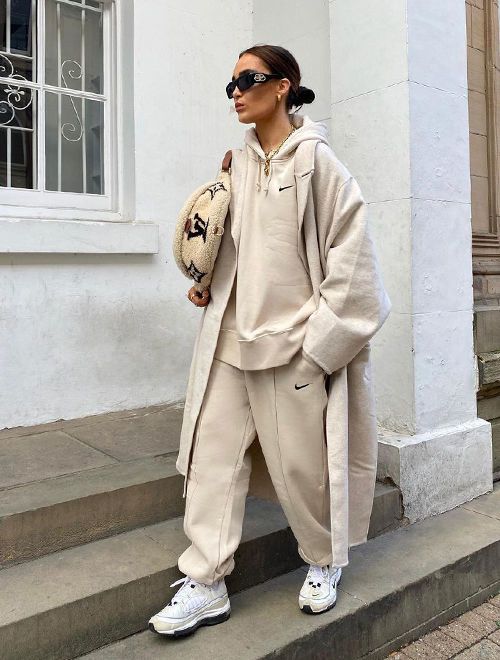 a neutral hoodie and sweatpants, white trainers, a neutral trench and a neutral printed bag for a comfy sporty look
