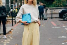 28 a stylish and delicate look with a touch of color, with a neutral oversized sweatshirt, yellow pleated pants, blue strappy shoes, a blue clutch