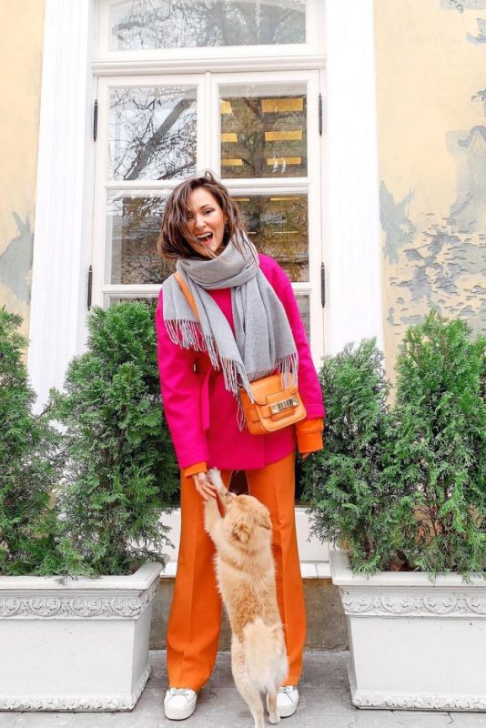 a bold spring outfit with a hot pink shirt jacket, orange trousers and a sweatshirt, a grey scarf, white platform sneakers